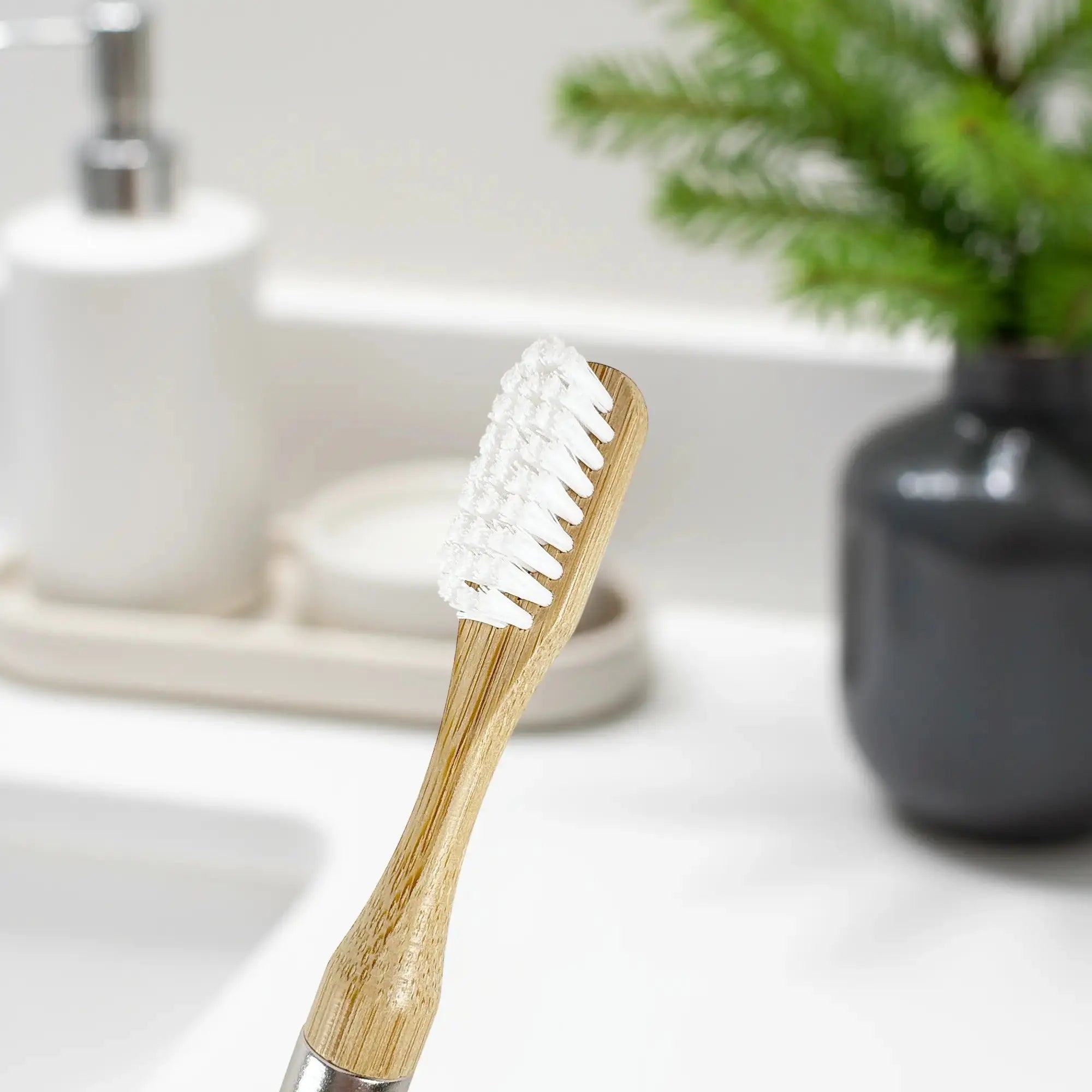 Close up of the Nathan and Sons Castor Oil Toothbrush Head featuring castor oil bristles and a bamboo neck with a blurred out background of a bathroom sink