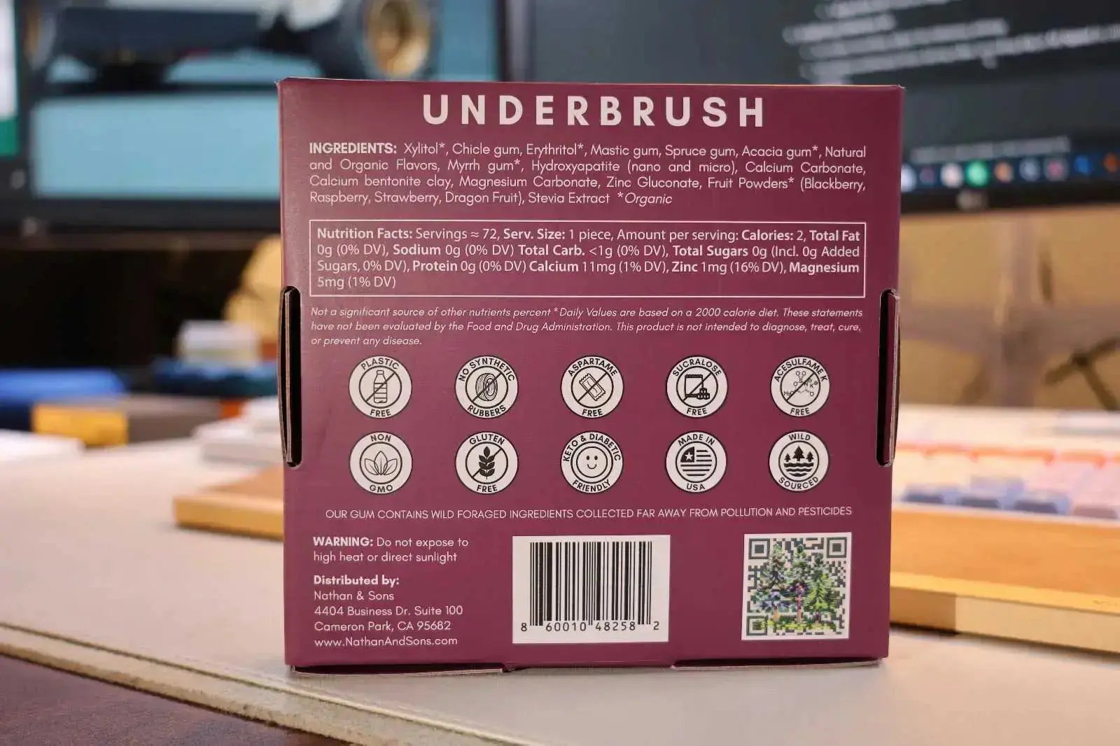 Close-up of the back of a Nathan & Sons Underbrush Remineralizing Gum box berry flavor, showing the ingredients list, nutrition facts, product claims (plastic free, no synthetic rubbers, aspartame free, sucralose free, acesulfame K free, non-GMO, gluten free, keto & diabetic friendly, made in USA, wild sourced), a barcode, a QR code, and distributor information
