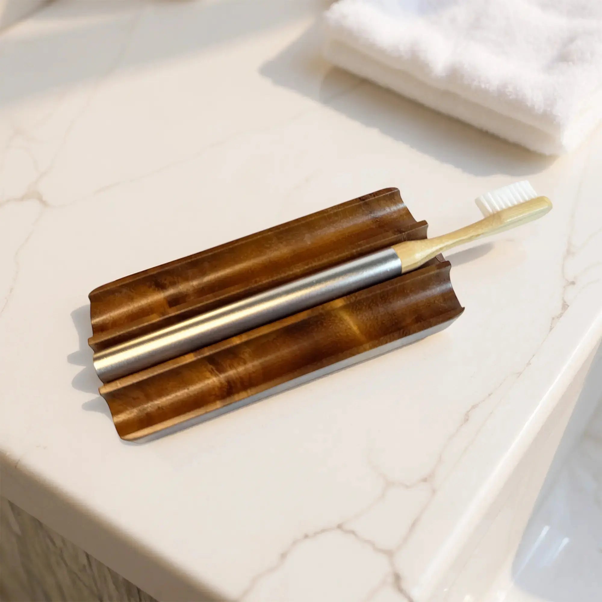 Nathan and Sons Castor Oil Toothbrush Kit featuring castor oil bristles, a bamboo neck and an aluminum handle resting on a sculpted wooden holder atop a marble bathroom countertop.