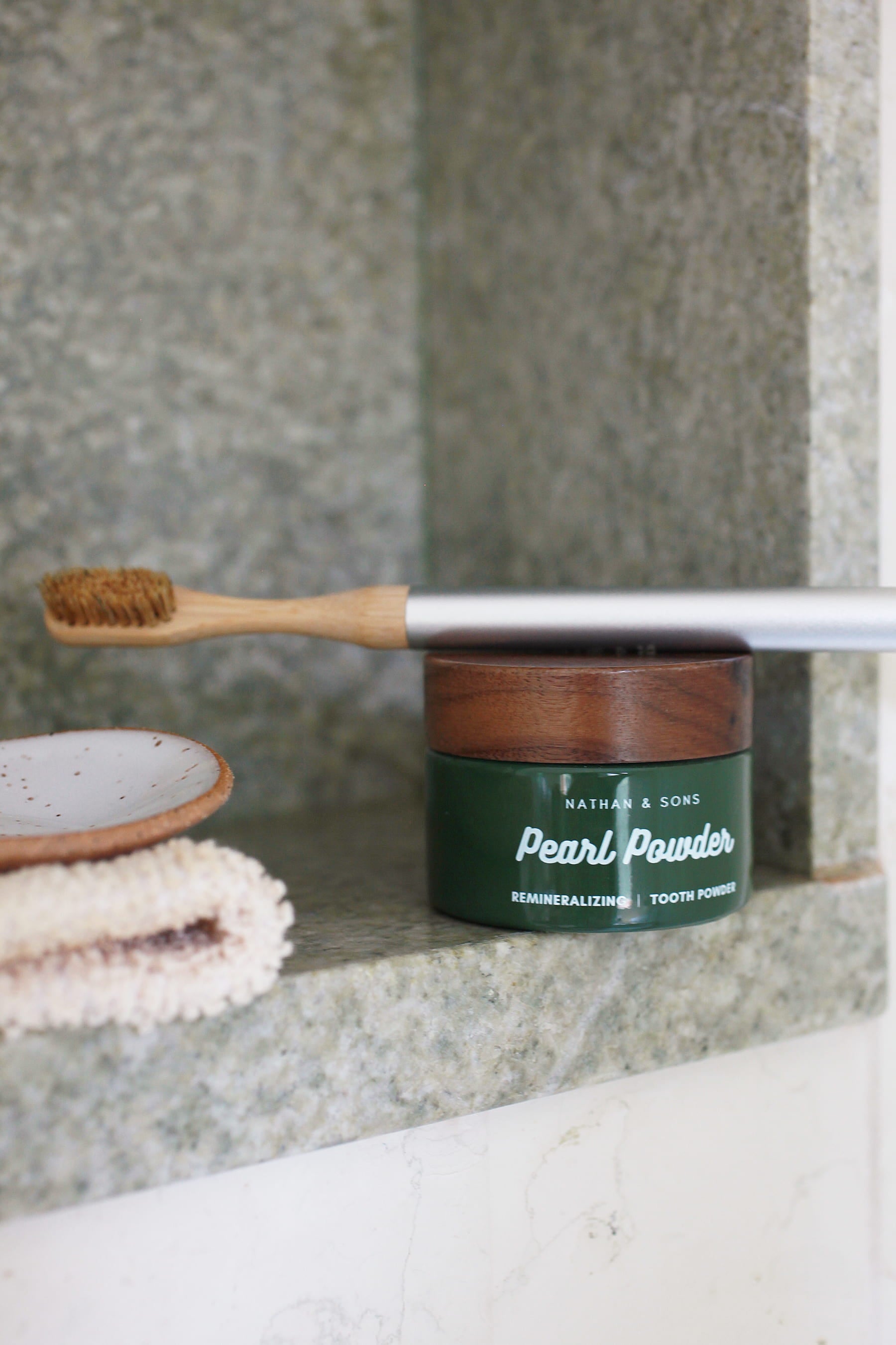 Jar of Nathan & Sons Pearl Powder Remineralizing Tooth Powder, with a Boars Hair Bamboo toothbrush resting on top.