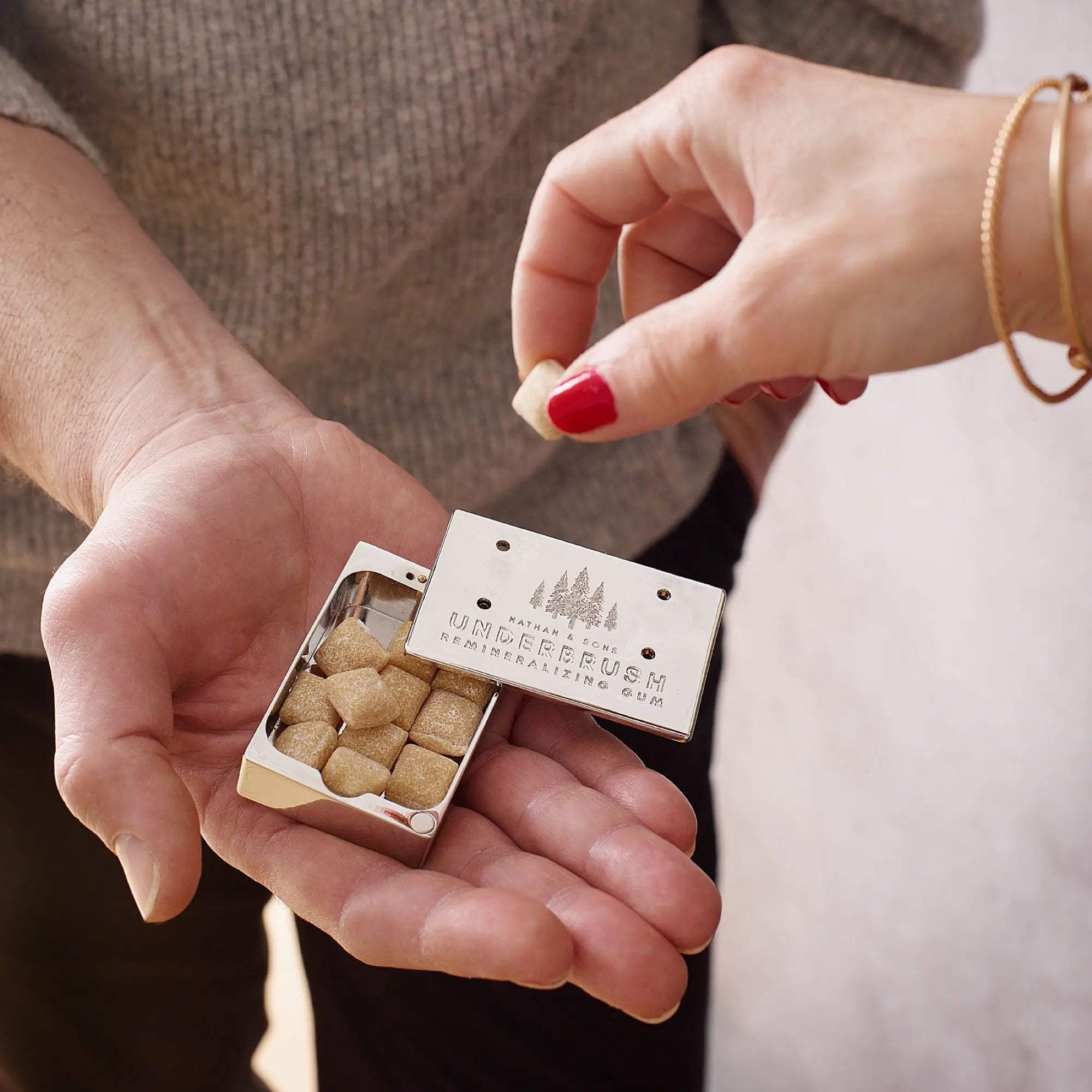 Hand taking Underbrush gum cube from Stainless Slide Snap Gum Case that is offered by another hand