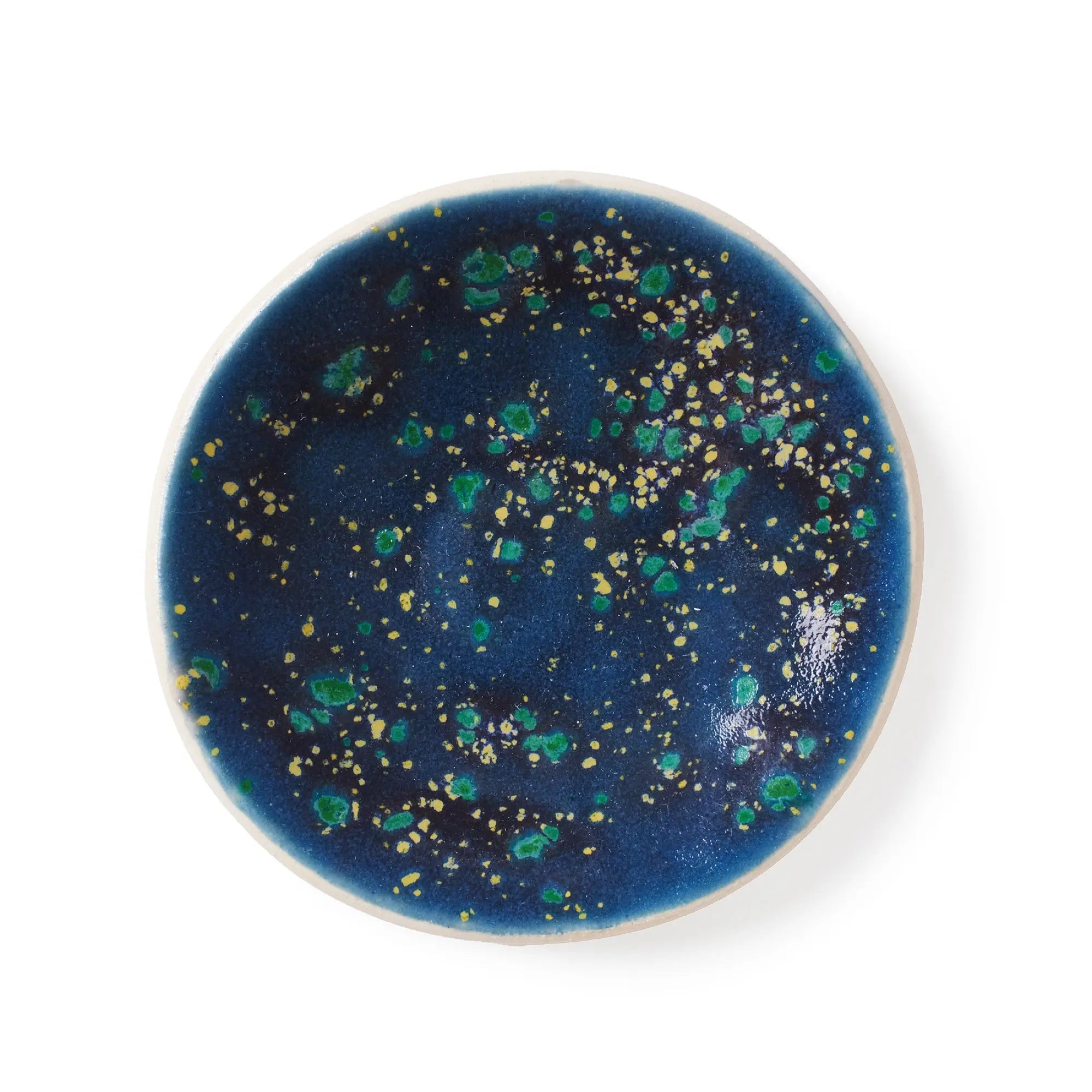 Top-down view of a handmade ceramic gum dish in a Blue Lagoon glaze, featuring a deep blue base with vibrant green and yellow speckles resembling a starry night sky or ocean reef