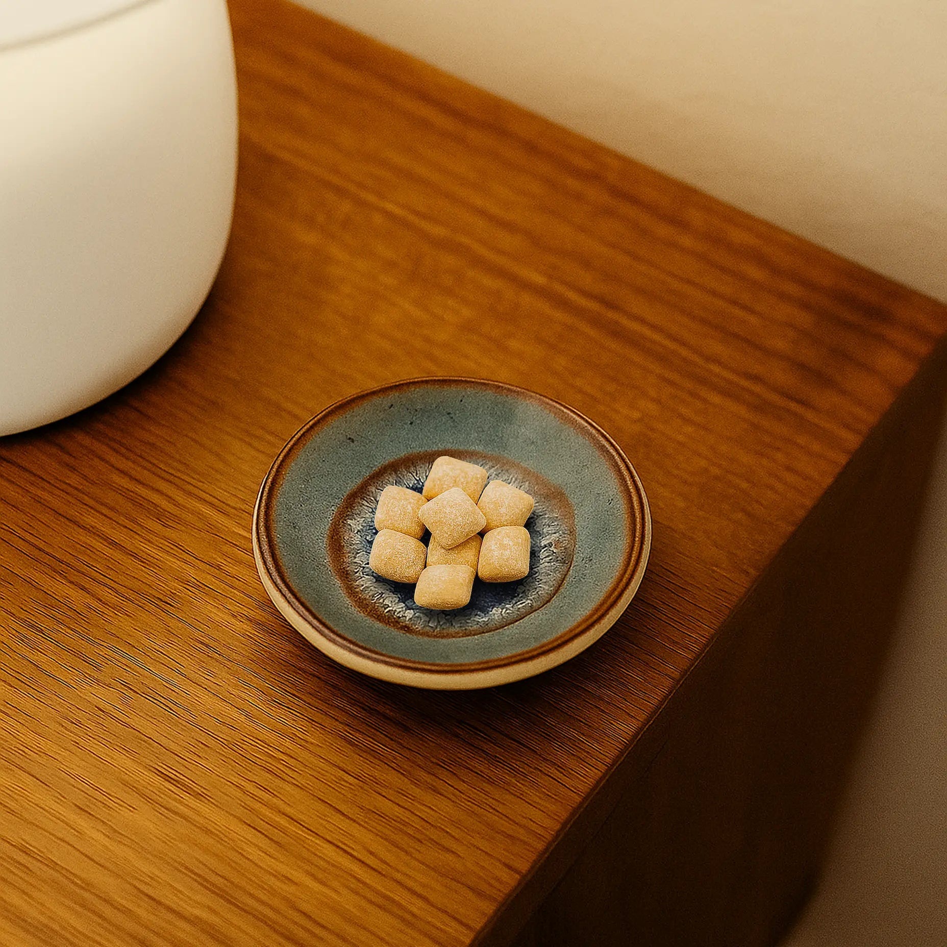 Underbrush handmade ceramic gum dish with a batik blue glaze flowing pattern holding a cluster of Underbrush remineralizing gum cubes, placed on a wooden bedside table