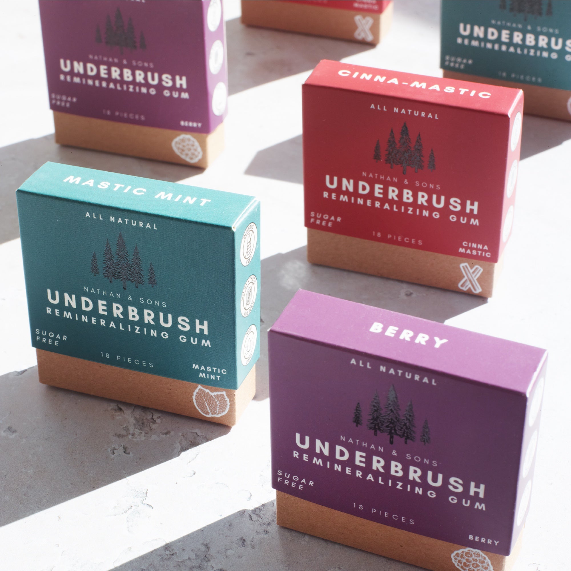 Boxes of xyitol chewing gum with mint, berry and cinnamon flavor, arranged upright, with sunlight streaming from behind.
