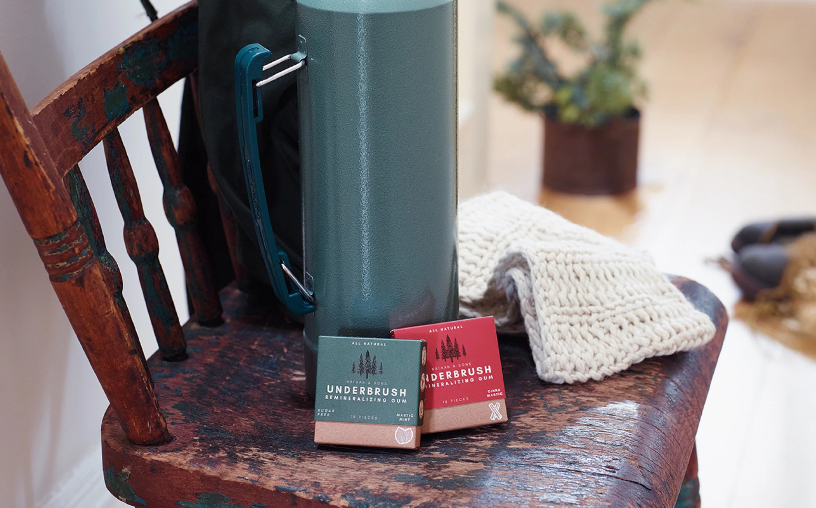 Underbrush mineralizing gum packs in Mastic Mint and Cinna-Mastic flavors displayed on a rustic wooden chair beside a thermos and winter knitwear