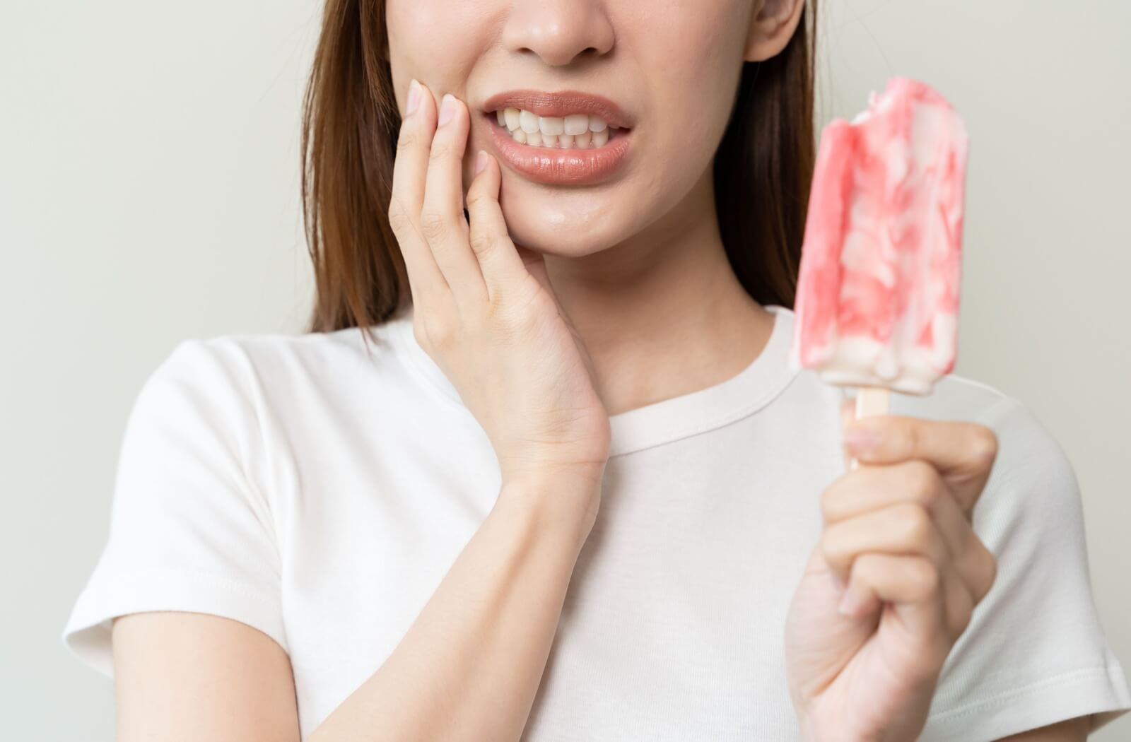 Woman experiencing tooth sensitivity while eating a cold popsicle