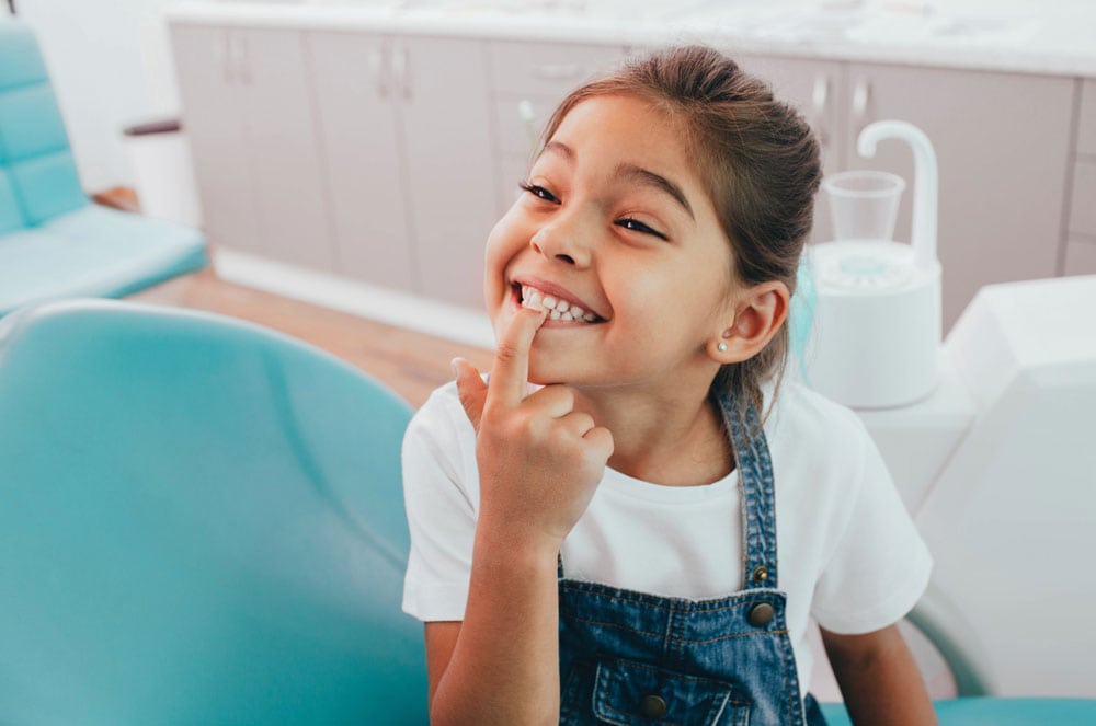 Smiling young girl pointing at her clean white teeth during a dental visit