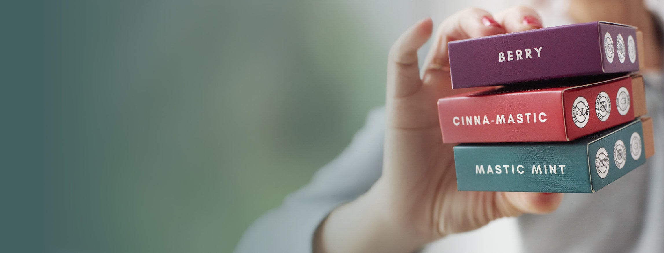 Hand holding stack of Underbrush natural chewing gum boxes in Berry, Cinna-Mastic, and Mastic Mint flavors